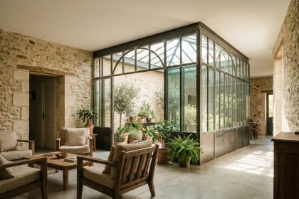 Véranda vitrée artisanale intégrée dans un salon français contemporain avec murs en pierre et sol en béton poli